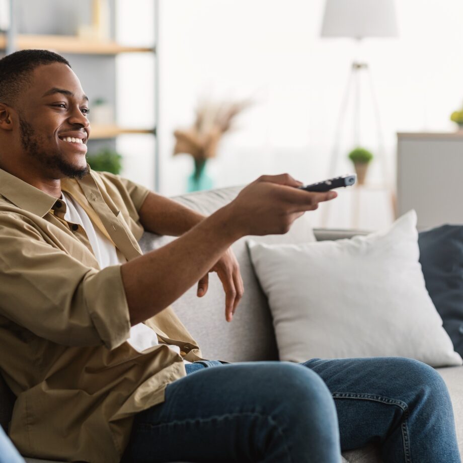 Happy African American Man Watching TV Switching Channels At Home